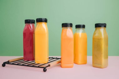 Şeffaf plastik şişelerde meyve ve sebze içecekleri. Yeşil, kırmızı, turuncu smoothie pembe-yeşil arka planda. Sağlıklı beslenme kavramı. Ön görünüm
