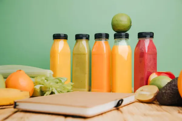 Fruit and vegetable smoothies in transparent plastic bottles. Green, red, orange smoothies on a green and wooden background. The concept of healthy eating. Front view