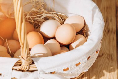 Farklı kahverengi ve bej tonlarda tavuk yumurtaları ahşap bir masada hasır bir sepet sarmaşıkta. Paskalya geçmişi. Üst görünüm