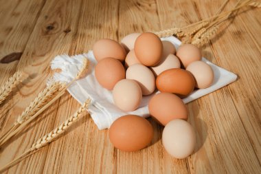 Farklı kahverengi ve bej renkte tavuk yumurtaları ahşap bir masada mutfak havlusunun üzerinde. Yumurta ve kuru buğday kulaklı Paskalya arkaplanı. Üst görünüm