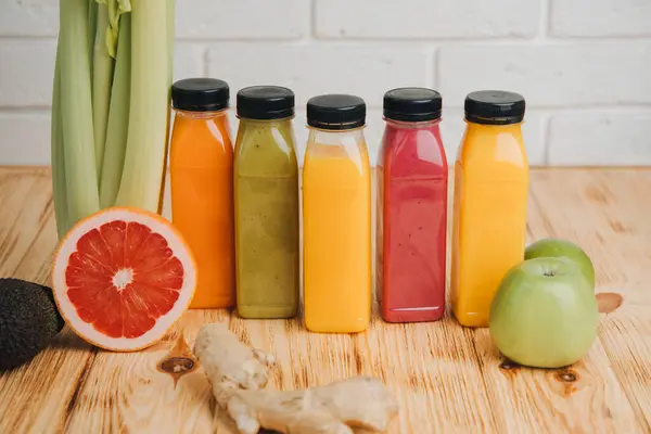 Fruit and vegetable smoothies in transparent plastic bottles. Red, green, orange smoothies on a wooden table. The concept of healthy eating. Front view