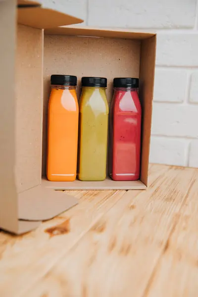Fruit and vegetable smoothies in transparent plastic bottles. Red, green, orange smoothies in cardboard box on a wooden table. The concept of healthy eating. Front view