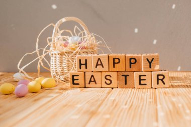 Paskalya arkaplan esprisi harfli tahta küpler. Ahşap bir arka planda, güneş yansımalı çok renkli çikolata süslemeli yumurtalar. Mutlu Paskalyalar. Ön görünüm