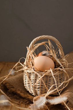 Farklı kahverengi ve bej tonlarda tavuk yumurtaları ahşap bir masada hasır bir sepet sarmaşıkta. Paskalya geçmişi. Ön görünüm