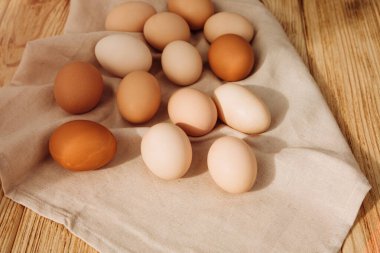 Gri mutfak havlusundaki ahşap arka planda farklı kahverengi ve bej renkte tavuk yumurtaları. Paskalya geçmişi. Üst görünüm