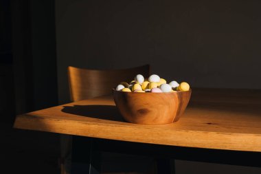 Ahşap bir masanın üzerinde, parlak gün ışığıyla kahverengi duvara yaslanmış, çok renkli çikolata süslemeli yumurtalar. Mutlu Paskalyalar. Ön görünüm