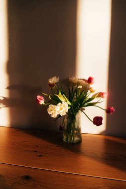 Tahta masadaki şeffaf vazoda beyaz ve pembe laleler. Bir buket çiçekle bahar arkaplanı. Ön görünüm
