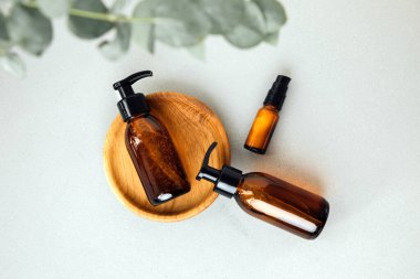 Gri beton arka planda okaliptüs dalı olan bir tepside yüz estetiği olan kehribar şişeleri, yüz temizleyici. Üst görünüm