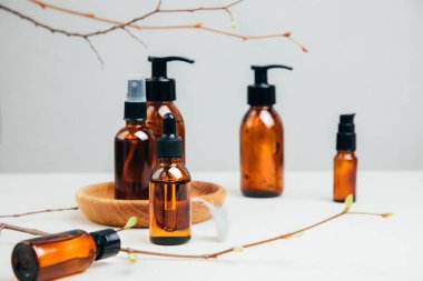 Doğal kozmetik seti. Yüz bakımı yapılmış kehribar şişeleri, beton arka planda banyo sıvısı ve ağaç dalları. Ön görünüm