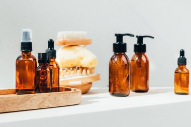 Doğal kozmetik seti. Yüz bakımlı kehribar şişeleri, beton zeminde banyo sıvısı ve doğal banyo süngeri. Ön görünüm