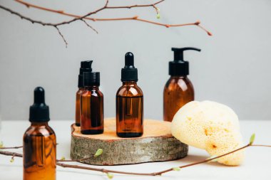 Doğal kozmetik seti. Yüz bakımı yapılmış kehribar şişeleri, beton arka planda banyo sıvısı ve ağaç dalları. Ön görünüm