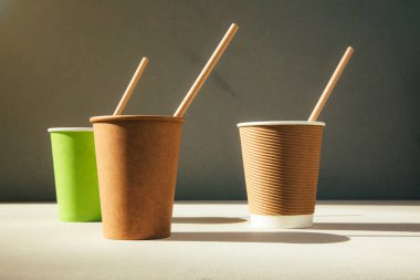 Kahverengi karton arka planda kağıt pipetli kağıt bardaklar. Çevre dostu, sıfır atık konsepti. Ön görünüm