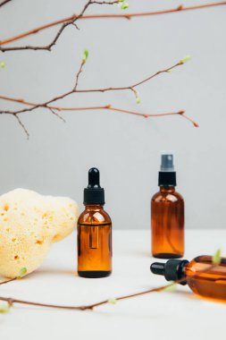 Doğal kozmetik seti. Yüz bakımı yapılmış kehribar şişeleri, beton arka planda banyo sıvısı ve ağaç dalları. Ön görünüm