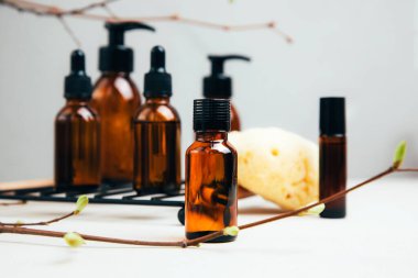 Doğal kozmetik seti. Yüz hatlarıyla kehribar şişeleri, beton arka planda elle yıkanan banyo sıvısı ve ağaç dalları. Ön görünüm