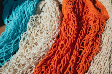 Güneşli bir günde kahverengi arka planda mavi, turuncu ve bej renkte tekrar kullanılabilir ağ torbaları. Ağ alışveriş torbaları. Sürdürülebilir kullanım kavramı