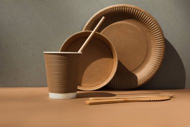 Kahverengi arka planda bir takım kağıt kap kacak ve ahşap çatal bıçak takımı. Çevre dostu, sıfır atık konsepti. Ön görünüm