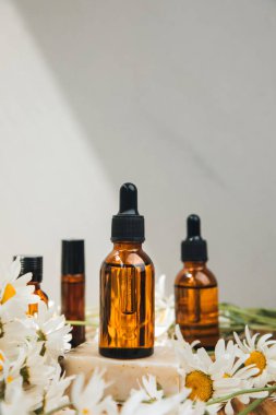 Doğal kozmetik seti. Kehribar şişeleri, yüz bakımı, banyo sıvısı beyaz papatya tarlası olan ahşap bir masada. Ön görünüm