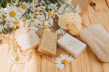 Doğal malzemelerden elde yapılan sabun, çeşitli otlar, papatya çayı. Sürdürülebilir kullanım kavramı, ahşap arka planda sarı havluda banyo ürünleri. Üst görünüm
