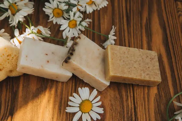 Doğal malzemelerden elde yapılan sabun, çeşitli otlar, papatya çayı. Sürdürülebilir kullanım kavramı, ahşap arka planda sarı havluda banyo ürünleri. Üst görünüm