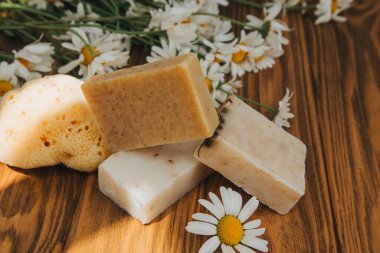 Doğal malzemelerden elde yapılan sabun, çeşitli otlar, papatya çayı. Sürdürülebilir kullanım kavramı, ahşap arka planda sarı havluda banyo ürünleri. Üst görünüm