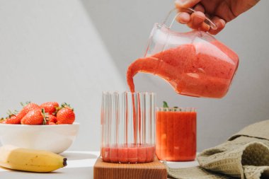Şeffaf bardaklarda meyve suyu. El, kırmızı bir çilekli içeceğe dökülüyor. Sağlıklı beslenme kavramı. Ön görünüm