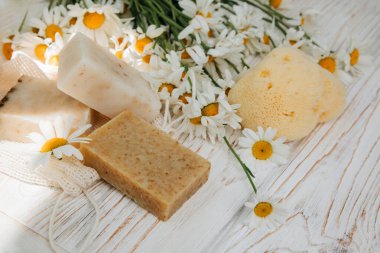 Doğal malzemelerden elde yapılan sabun, çeşitli otlar, papatya çayı. Sürdürülebilir kullanım kavramı, beyaz ahşap arka planda banyo ürünleri. Üst görünüm