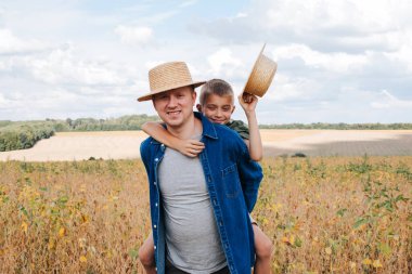 Agronomist, baba ve oğul soya fasulyesi tarlasında birlikte. Neşeli adam sırtında bir oğul taşıyor. Babam güneşli yürür