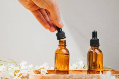 Doğal kozmetik seti. Kehribar şişeleri, yüz bakımı, banyo sıvısı beyaz papatya tarlası olan ahşap bir masada. Ön görünüm