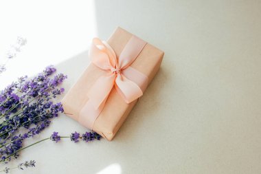 Selamlaşmak için arka plan. Hafif beton arka planda lavanta çiçekleri olan yumuşak pembe kağıda sarılmış bir hediye. Üst görünüm