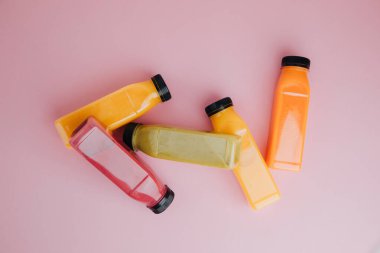 Şeffaf plastik şişelerde meyve ve sebze içecekleri. Pembe arka planda kırmızı, yeşil, turuncu meyve püresi. Sağlıklı beslenme kavramı. Üst görünüm
