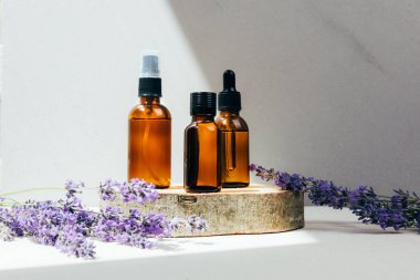 Doğal kozmetik seti. Yüzünde kehribar şişeleri, beton arka planda lavanta çiçekleriyle banyo sıvısı. Ön görünüm