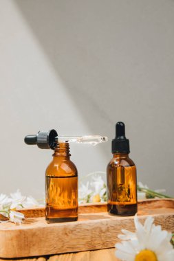 Doğal kozmetik seti. Kehribar şişeleri, yüz bakımı, banyo sıvısı beyaz papatya tarlası olan ahşap bir masada. Ön görünüm