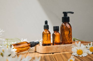 Doğal kozmetik seti. Kehribar şişeleri, yüz bakımı, banyo sıvısı beyaz papatya tarlası olan ahşap bir masada. Ön görünüm