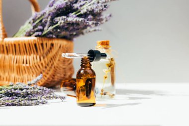 Lavanta yağı ve açık kehribar kozmetik şişesi açık arkaplanda parlak bir güneş ışığında lavanta çiçekleri. Ön görünüm