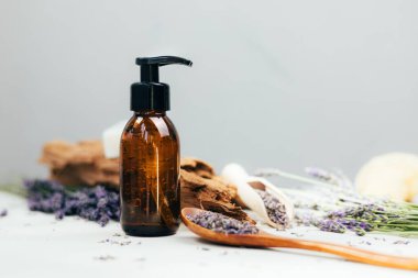 Doğal kozmetik seti. Yüzünde kehribar şişeleri, beton arka planda lavanta çiçekleriyle banyo sıvısı. Ön görünüm
