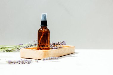 Doğal kozmetik seti. Yüzünde kehribar şişesi, beton arka planda lavanta çiçekleri olan banyo sıvısı. Ön görünüm