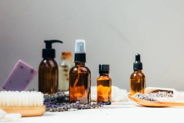 Doğal kozmetik seti. Yüzünde kehribar şişeleri, beton arka planda lavanta çiçekleriyle banyo sıvısı. Ön görünüm