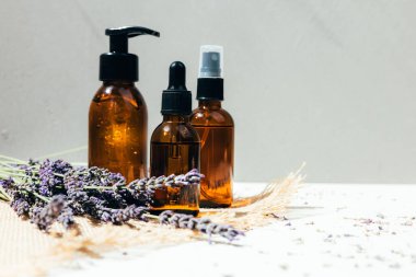 Doğal kozmetik seti. Yüzünde kehribar şişeleri, beton arka planda lavanta çiçekleriyle banyo sıvısı. Ön görünüm