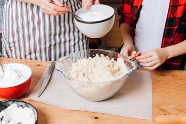 Anne ve oğlu mutfaktaki tahta masada kurabiye için hamur hazırlıyorlar. Evde yemek pişirme tatlısı. Çocuklarla ortak aktiviteler. Üst görünüm