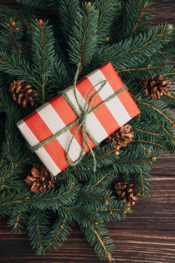 Noel, şenlikli bir geçmiş. Kahverengi ve kırmızı hediye kutusu, yeşil kozalaklı dallarda, ahşap bir arka planda. Üst görünüm