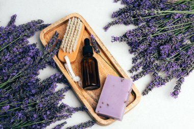 Doğal kozmetik seti. Kehribar şişeleri, yüz, banyo sıvısı ve lavanta sabunu beton bir arka planda, lavanta çiçekleri olan ahşap tepside. Üst görünüm