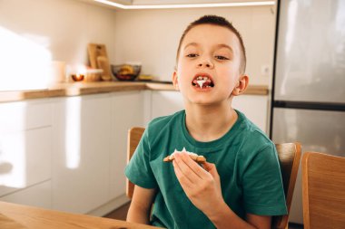 Mutfakta okul çağındaki bir çocuk güneşli havada Noel kurabiyeleri süslüyor. Çocuklar mutfakta, ev yapımı pastalar. Ön görünüm