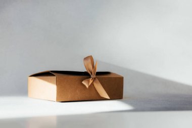Selamlama arka planı. Gri arka planda kahverengi hediye kutusu ve fotokopi alanı. Ön görünüm