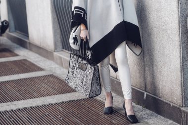 Milan, Italy - February 25, 2022: Crop anonymous female in trendy outfit with ornamental pattern on Etro handbag standing near concrete wall.