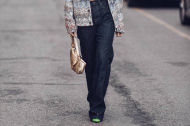 Milan, Italy - February 25, 2022: Female in jeans and crop top with ornamental jacket and stylish bag walking on city street of Milan.