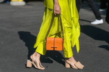 Milan, Italy - February 26, 2022: Female in stylish bright yellow asymmetrical pants with orange bag and beige sandals.