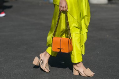 Milan, Italy - February 26, 2022: Female in stylish bright yellow asymmetrical pants with orange bag and beige sandals.