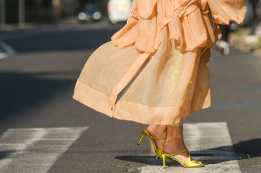 Milan, Italy - February 25, 2022: Unrecognizable female in stylish pink dress and high heeled sandals walking on crosswalk on sunny day on city street