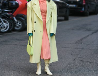 Milan, Italy - February 24, 2022: Woman wearing trendy coat pink dress green gloves and beige boots with yellow handbag