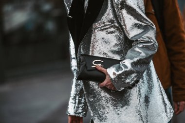 Milan, Italy - February 24, 2022: Crop anonymous trendy person in silver jacket with black handbag walking on street in Milan
